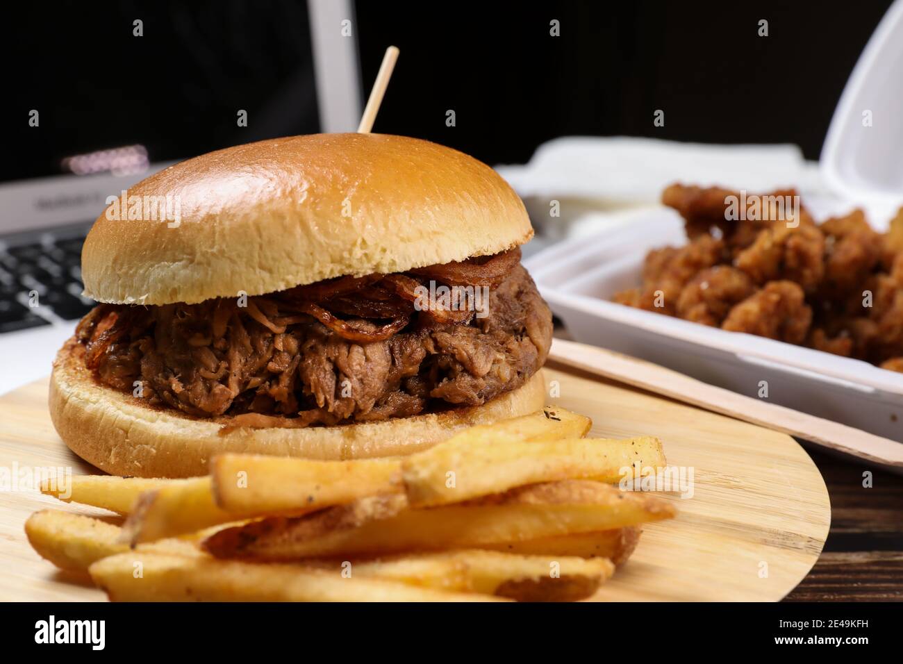 Frisch gekochter Rindfleisch-Burger mit pommes Frites vor dem Laptop vor schwarzem Hintergrund. Lieferung von Lebensmitteln zu Hause. Stockfoto