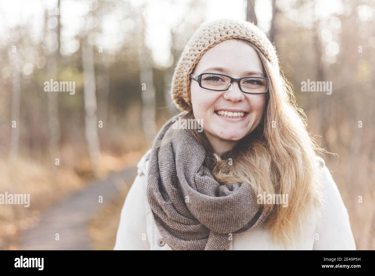 Lächelndes und glückliches Gesicht einer jungen Frau mit Brille im Freien Im Herbst mit Bäumen im Hintergrund Stockfoto