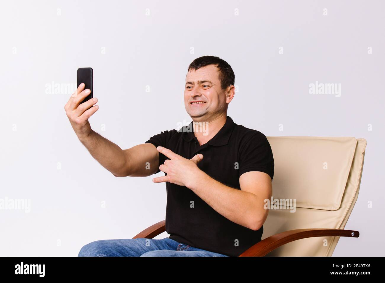 Der ältere Mann sitzt in einem Ledersessel und kommuniziert online per Video über nonverbale Zeichen, lächelnd. Weißer Hintergrund. Stockfoto