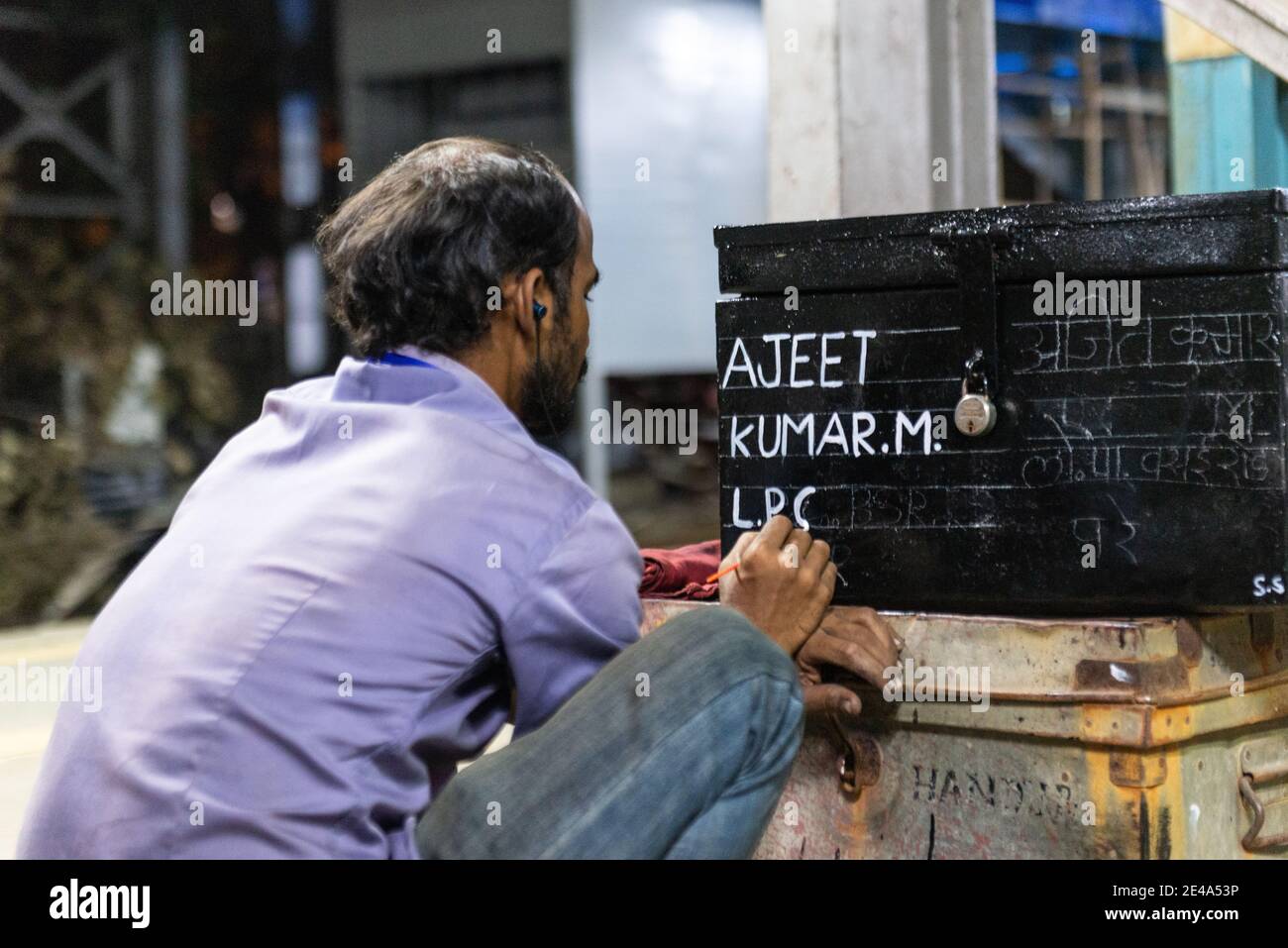 Bahnhofsmitarbeiter, die den Namen des neu beigetretenen Lokopiloten auf einem Linienkastenstamm an der Vasai Road Station, Maharashtra, Indien schreiben Stockfoto