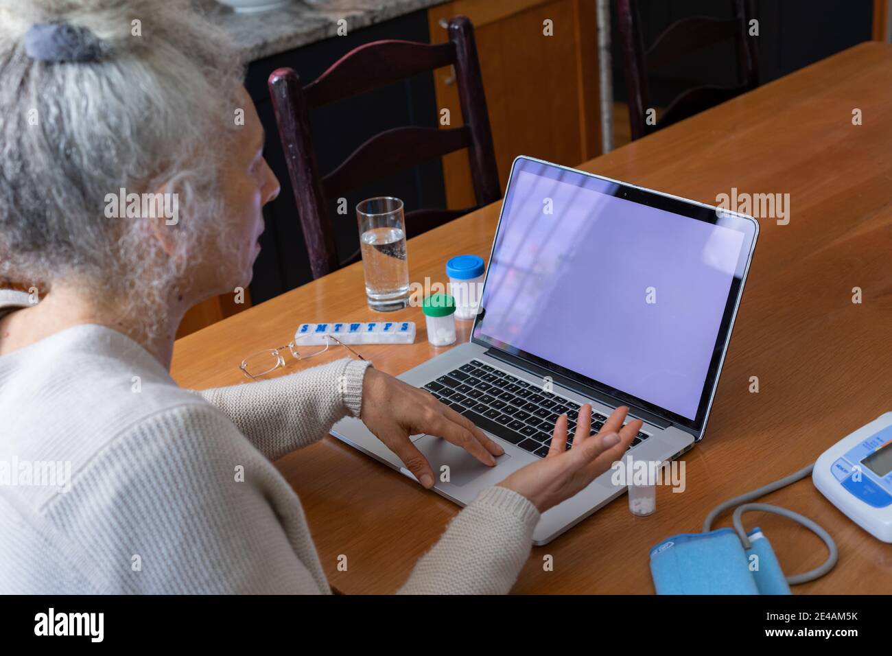 Ältere kaukasische Frau mit Videoanruf medizinische Beratung mit Laptop In der Küche Stockfoto