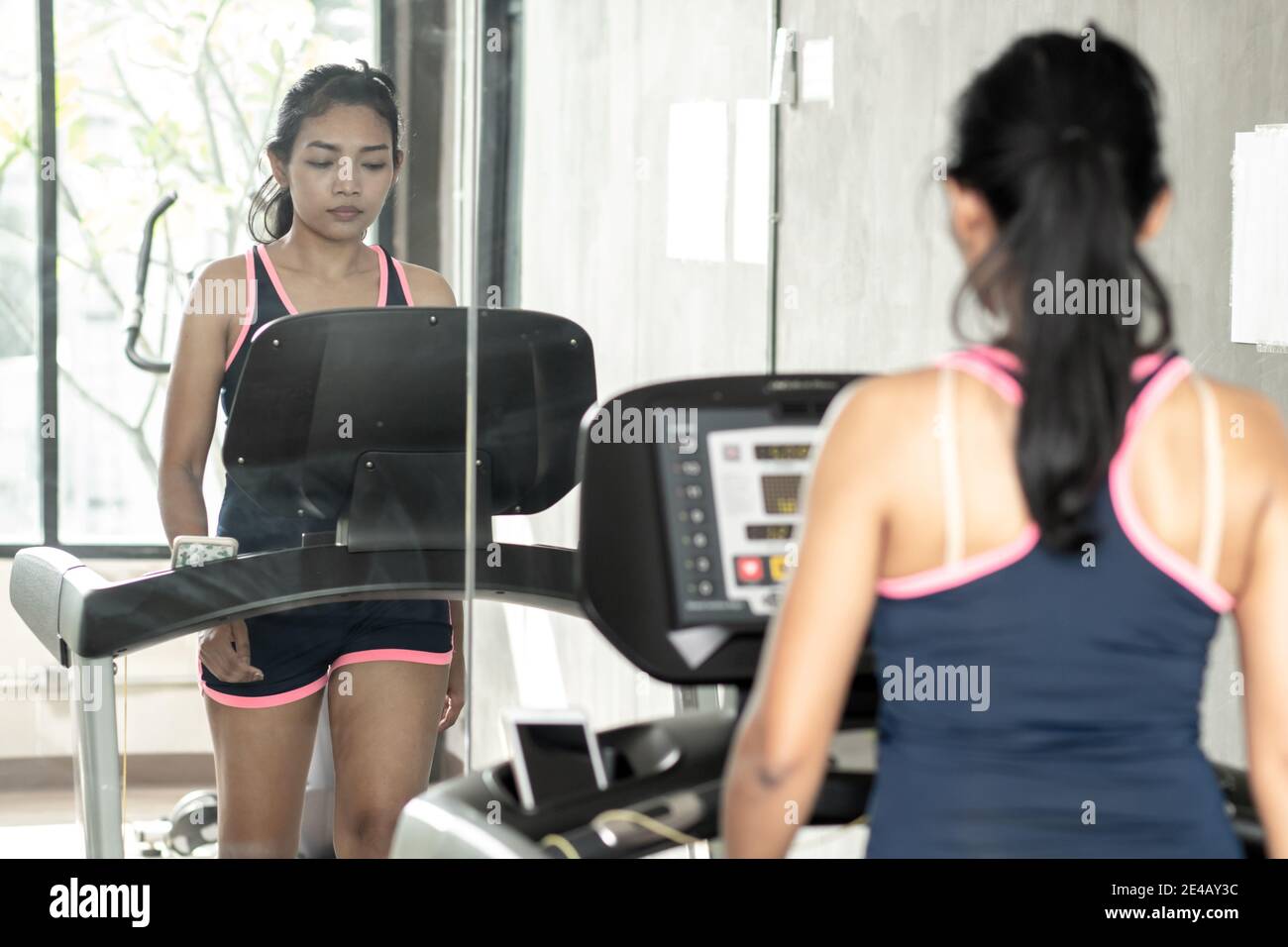 Junge Frau, die im Fitnessstudio mit Spiegeln praktiziert. Mädchen, die auf dem Laufband im Fitnessclub spazieren gehen. Stockfoto