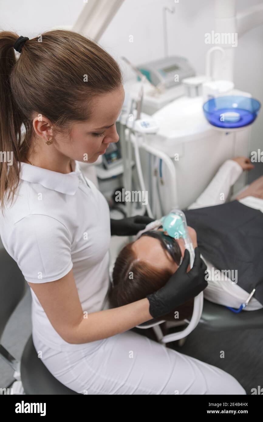 Vertikale Aufnahme eines professionellen Zahnarztes, der eine Inhalationssedierung ansetzt Maske auf ihre Patientin Stockfoto