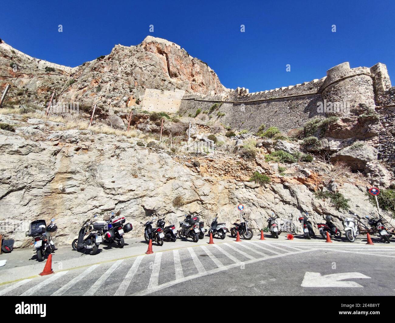 Die Festungsmauer überragt den Parkplatz für Zweiräder vor der Unterstadt Monemvasia, Lakonien, Peloponnes, Griechenland Stockfoto
