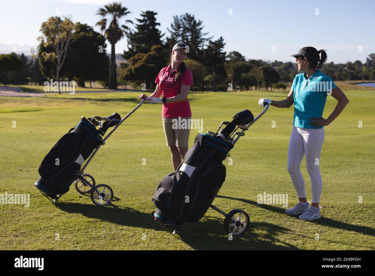 Zwei kaukasische Frauen auf dem Golfplatz mit Golftaschen und Sprechen Stockfoto