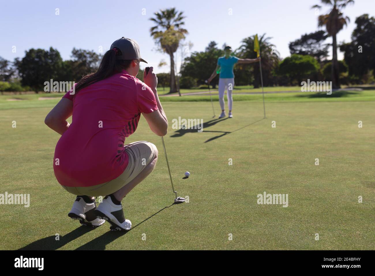 Zwei kaukasische Frauen spielen Golf, eine hockt, bevor sie ein Schuss auf das Loch Stockfoto