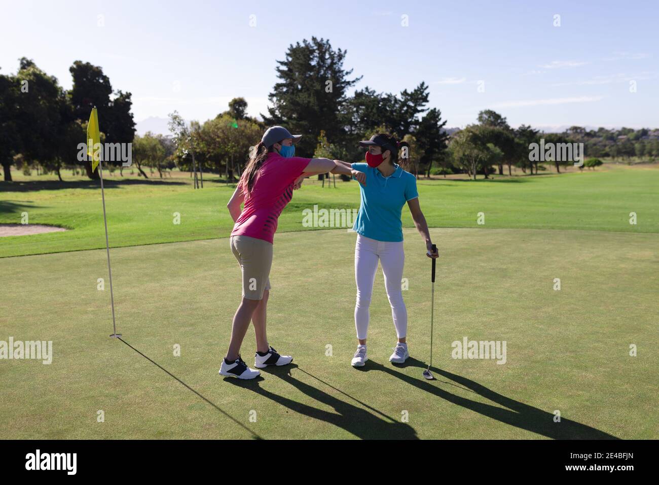 Zwei kaukasische Frauen mit Gesichtsmasken spielen Golf stoßen Ellenbogen Stockfoto