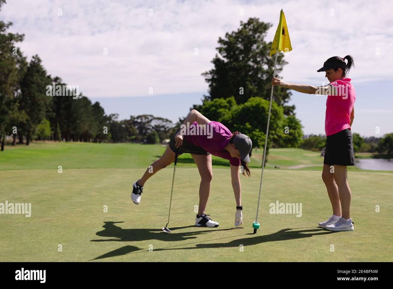 Zwei kaukasische Frauen spielen Golf, eine hält Flagge, die eine nimmt Kugel aus Loch Stockfoto
