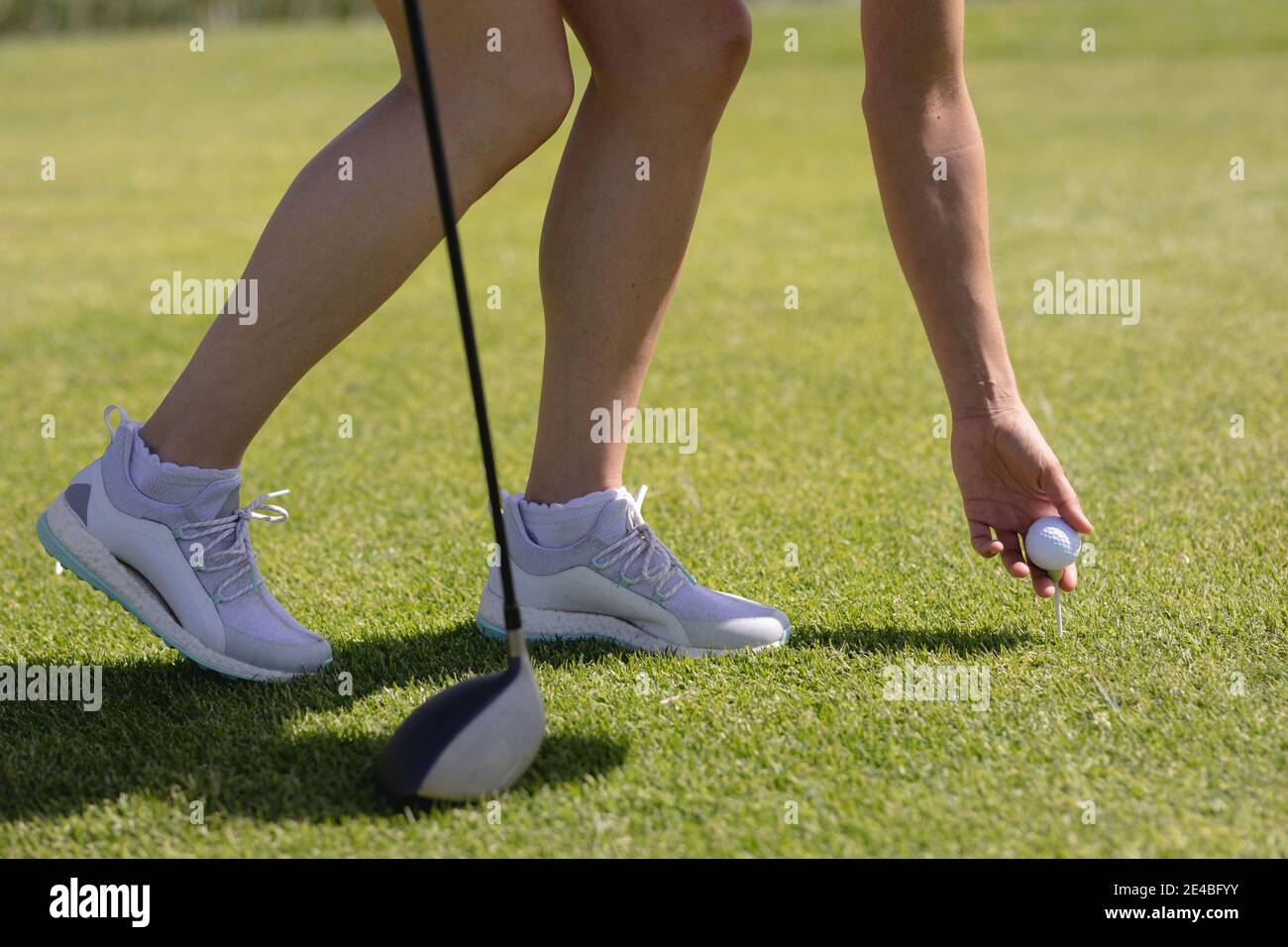 Unterer Abschnitt der kaukasischen Frau, die Golf spielt und sich zum Platz neigt Ball vor dem Schuss Stockfoto