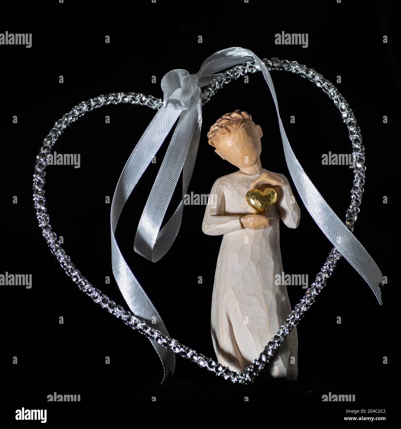 Weidenbaum Figur einer Dame hält ein goldenes Herz in einem größeren silbernen Herz, die das Thema der Liebe auf einem schwarzen Hintergrund. Stockfoto