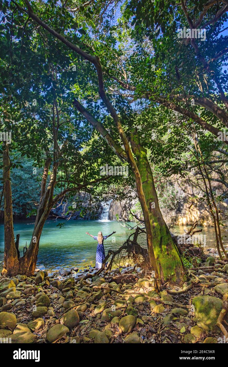 Eine Frau (MR), umgeben von Bäumen, steht in einem Teich mit einem Wasserfall in einem tropischen Dschungel auf der Insel Maui, Hawaii. Stockfoto