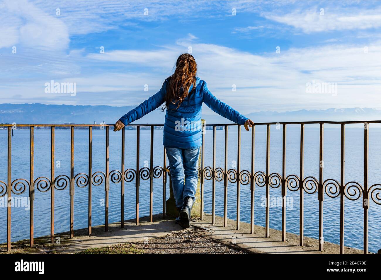 Frau in einer blauen Daunenjacke auf dem Geländer vorbei Ein See Stockfoto