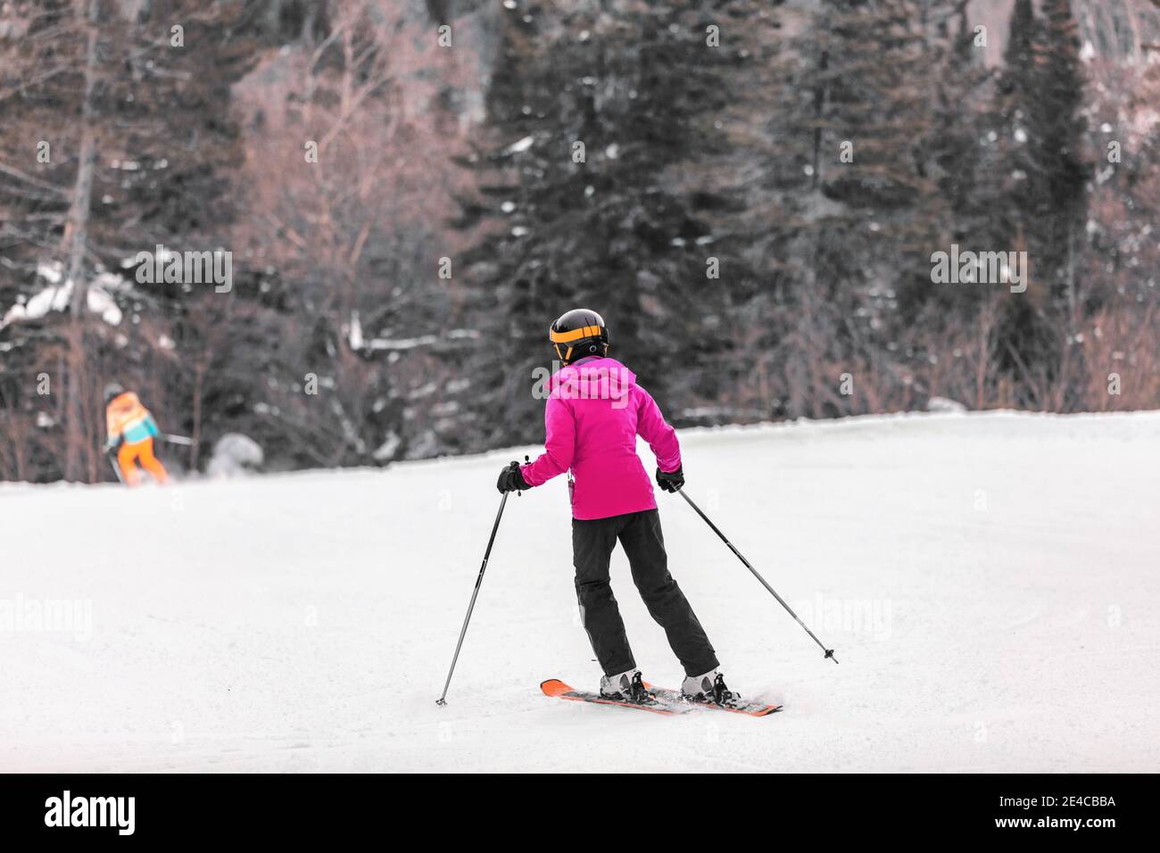 Skifahrer Frau Skifahren lernen, auf Berghang Skifahren. Wintersport Outdoor-Aktivitäten. Mädchen von hinten in rosa Jacke und Brille, Helm, Skier, Stöcke Stockfoto