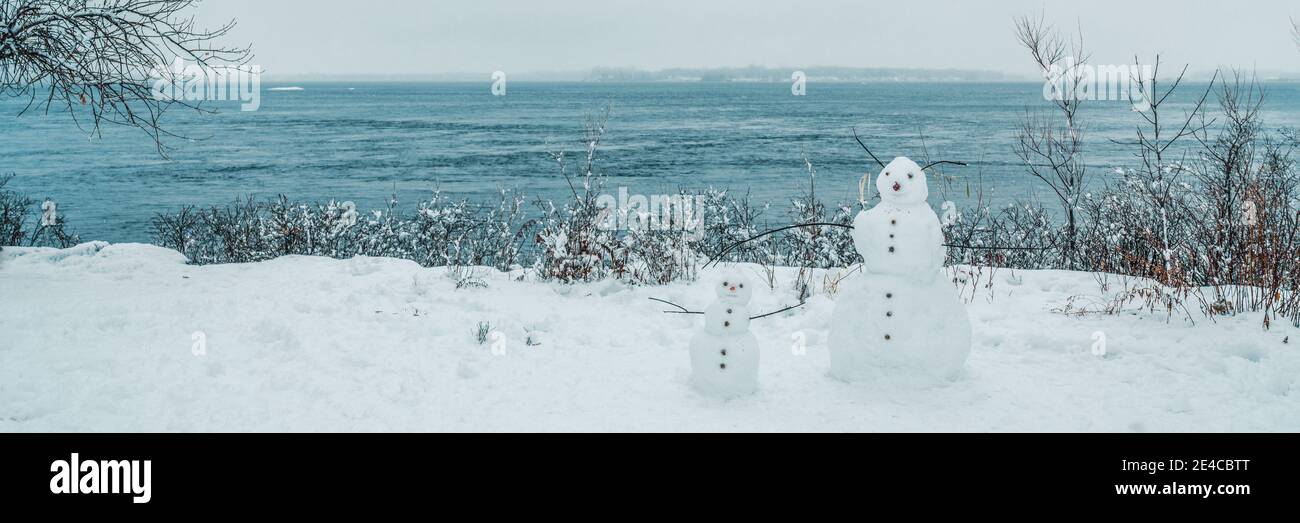 Winterlandschaft Spaß Outdoor-Aktivitäten für Kinder, Bau Schneemann im Schnee in Quebec, Kanada. Banner zum Naturspaß. Zwei Schneemänner vor dem Wasser Stockfoto