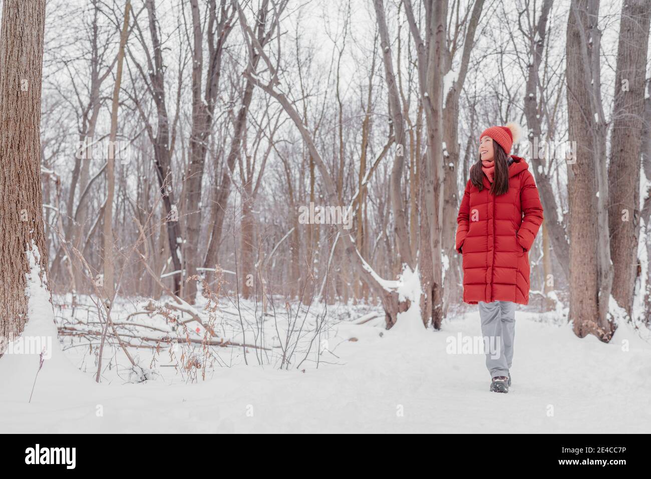 Glücklich asiatische Mädchen zu Fuß in Schnee Pfad. Frau im roten Mantel macht Outdoor-Winteraktivitäten genießen kalte Jahreszeit Stockfoto