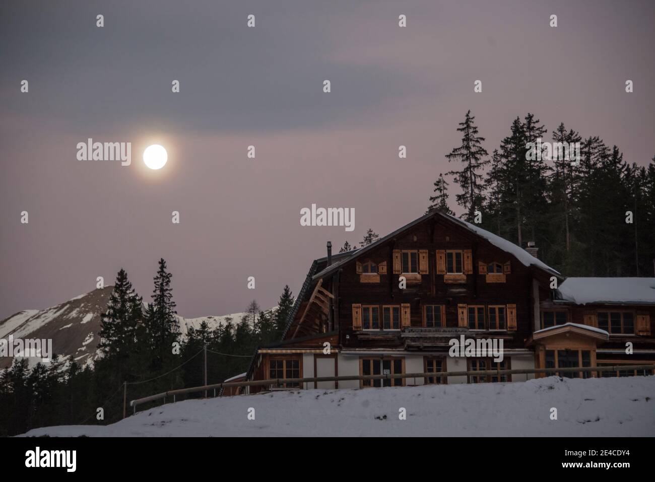 Vollmond bei Sonnenaufgang in den winterlichen Bergen mit Berg Station Stockfoto