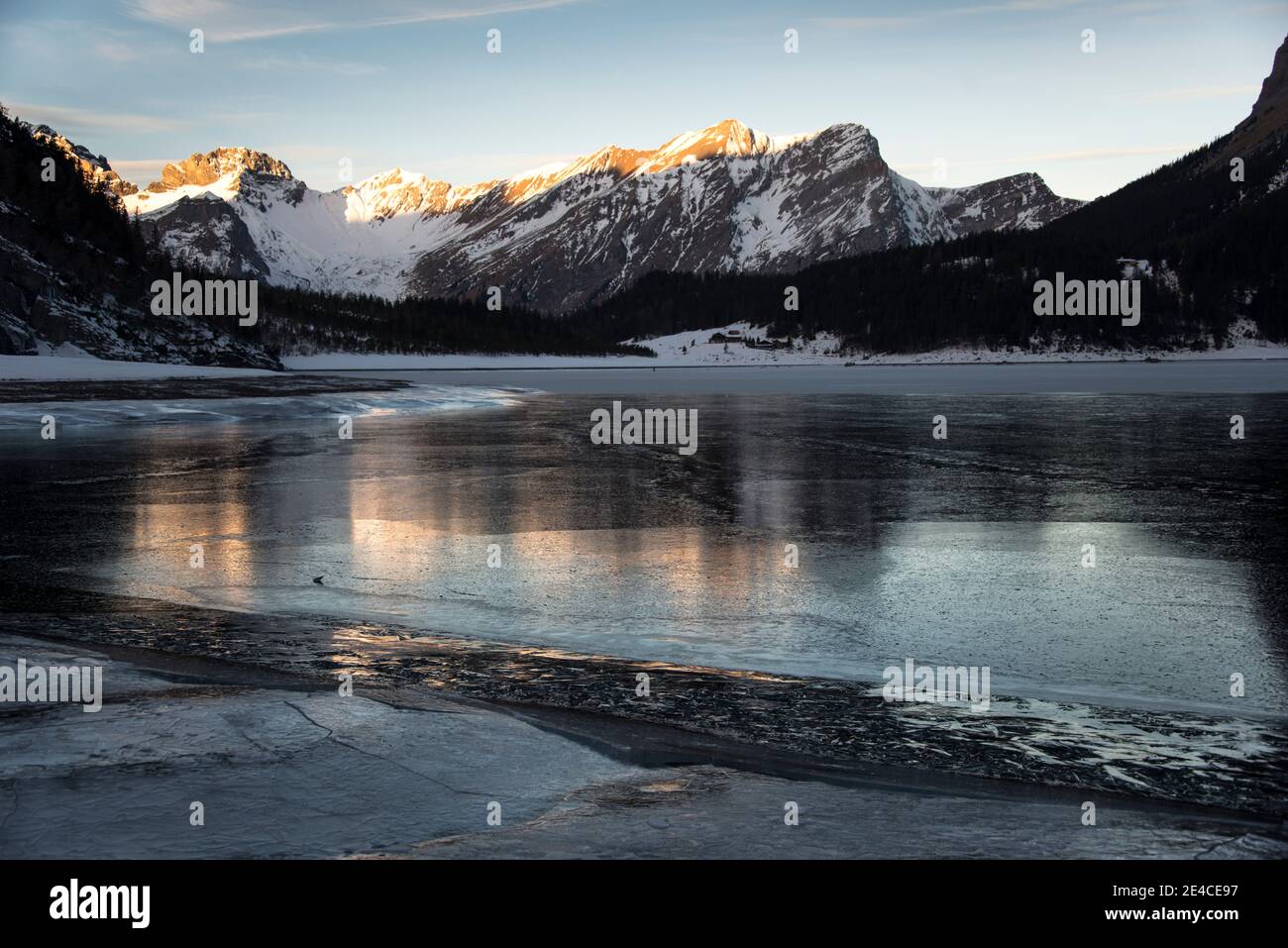 Gefrorener Bergsee im Morgengrauen erleuchten die ersten Sonnenstrahlen die Gipfel Stockfoto