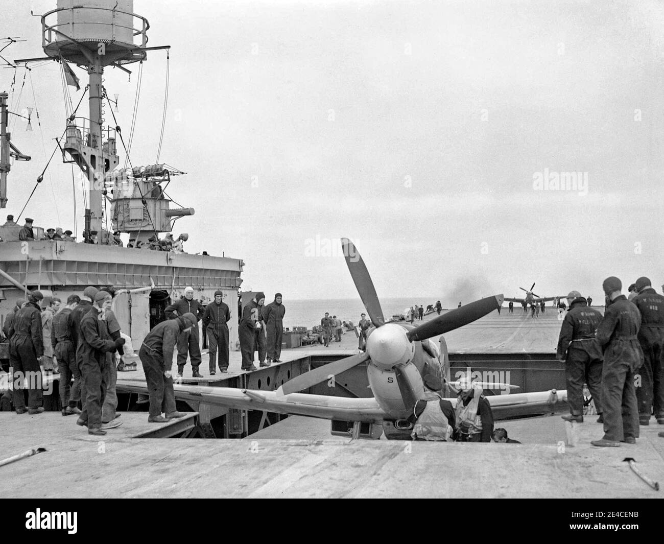 Ein Supermarine Seafire wird mit einem Aufzug zum Flugdeck von HMS Furious gebracht. Ein weiteres Flugzeug ist am anderen Ende des Flugdecks zu sehen, 1944 Stockfoto
