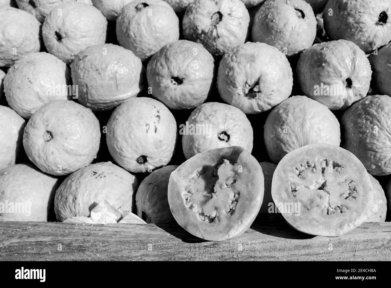 Zwei Hälften lebendiger Gavas-Früchte öffneten sich mit einem Stapel Von mehr Früchten dahinter [Schwarz-Weiß-Version] Stockfoto