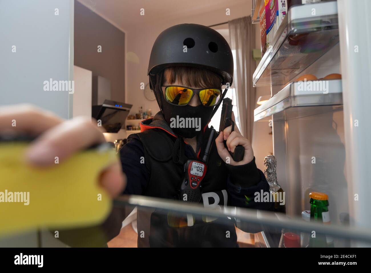 Boy in Helm, Sonnenbrille und FBI-Shirt reinigt den Kühlschrank Stockfoto