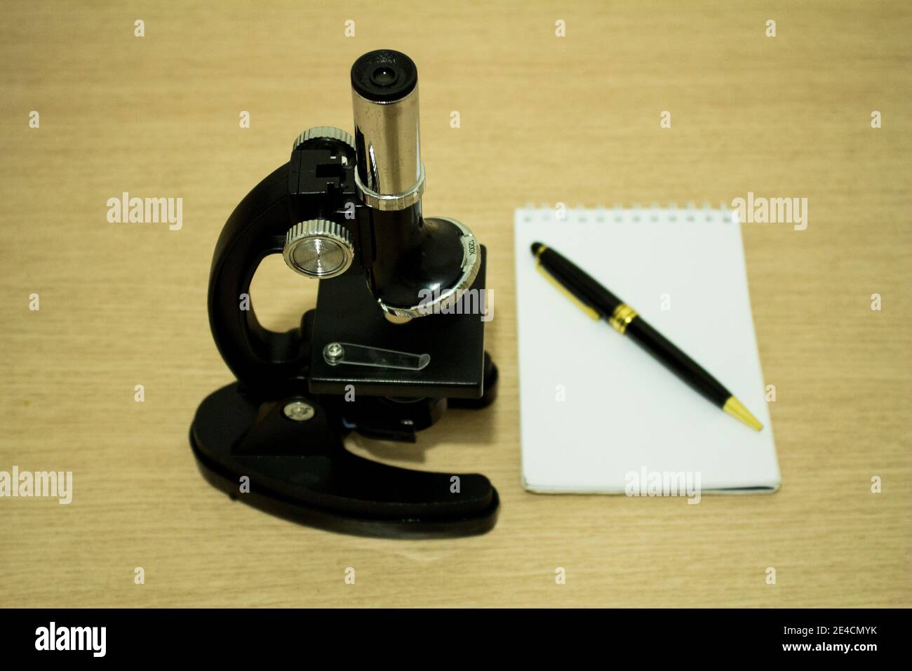 Schwarzes Mikroskop über dem Schreibtisch mit einem Notebook und einem Stift daneben Stockfoto