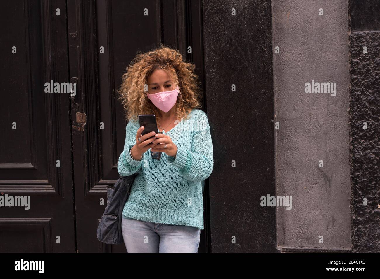 Erwachsene Frau tragen Schutzmaske gegen covid-19 Coronavirus Virus Notfall - Schützen Sie sich Menschen mit Anti-Virus-Zubehör - weiblich In der Stadt mit Telefon lesen Nachrichten über Gesundheit Stockfoto