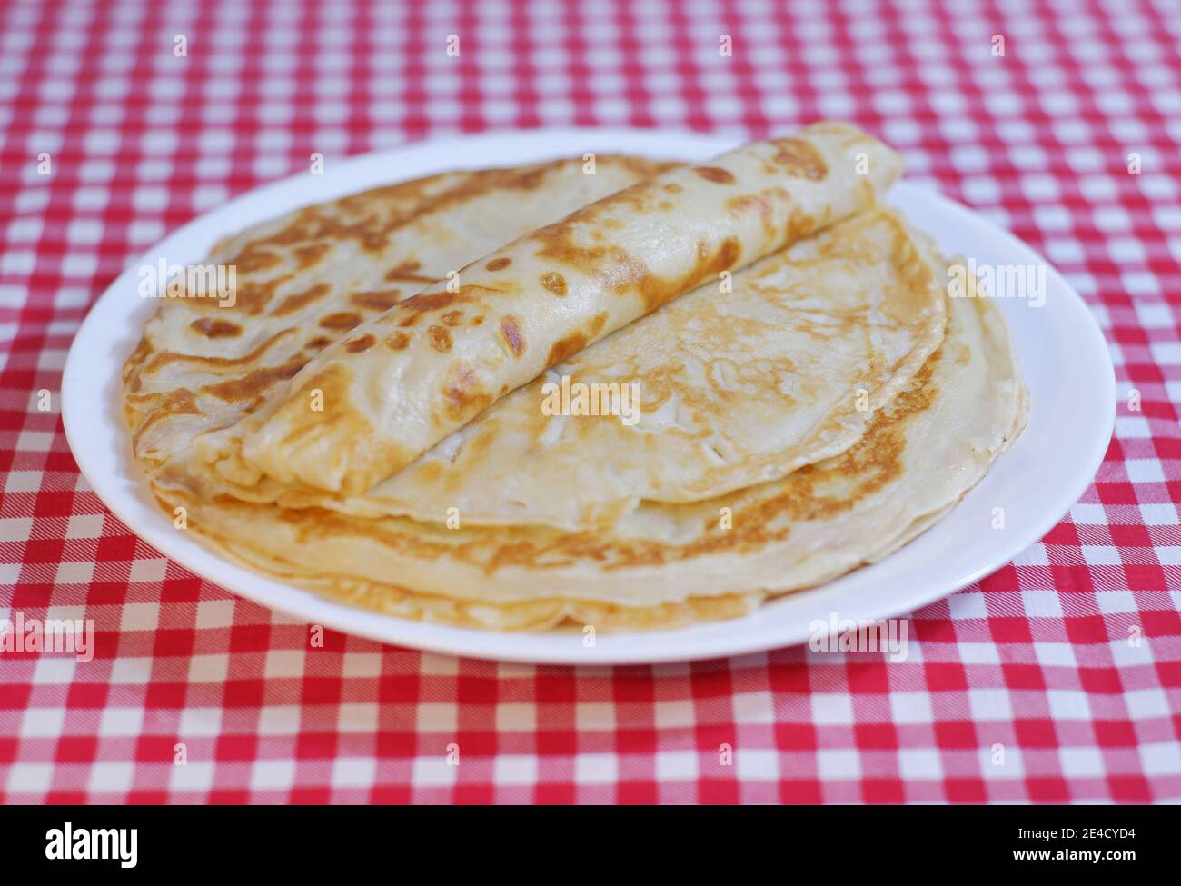 Köstliche gebratene Shrovetide-Pfannkuchen stapeln sich auf einem Teller auf einer karierten Tischdecke. Stockfoto