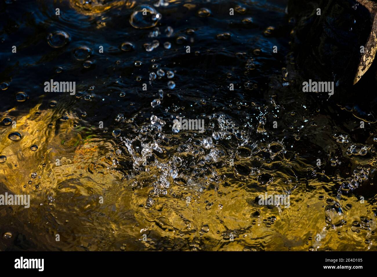 Wassertropfen, die ins Wasser auslaufen; starker Kontrast von hell und dunkel Stockfoto