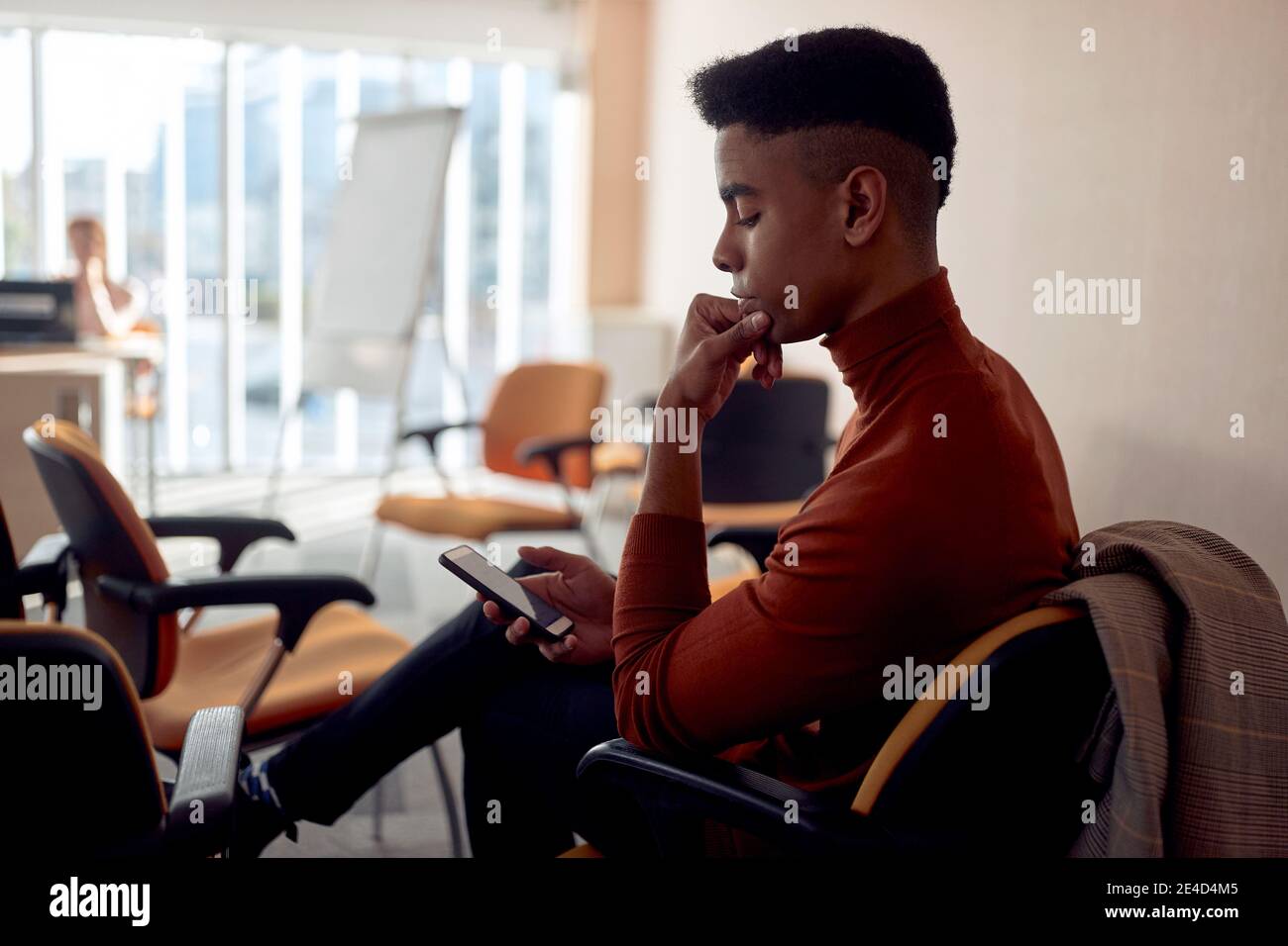 Junger afroamerikanischer Geschäftsmann, der sein Handy anschaut, denkt, allein sitzt Stockfoto