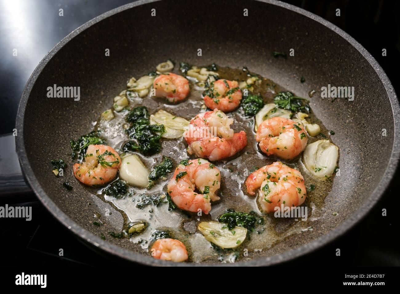 Shrimps oder schwarze Tiger Garnelen werden mit Olivenöl, Knoblauch und Petersilie in einer Pfanne für einen leckeren Meeresfrüchte-Snack, ausgesuchter Fokus, schmaler Absauch sautiert Stockfoto