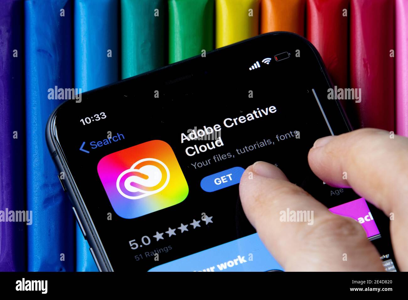Mobile Adobe Creative Cloud-App im AppStore mit einem bunten Hintergrund aus Plastilin. Installation der Creative Cloud auf dem iPhone. Stockfoto