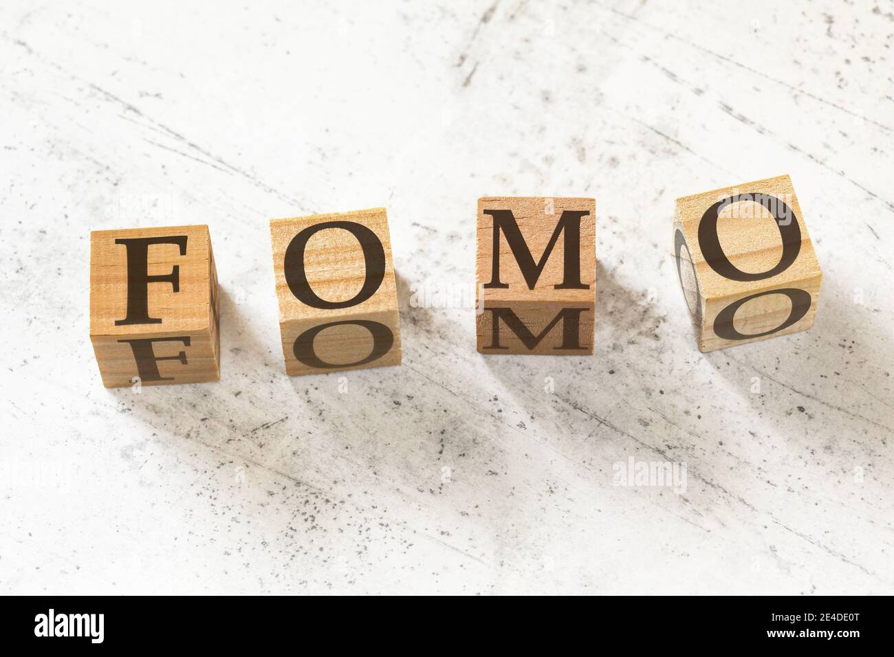 Vier Holzwürfel mit den Buchstaben FOMO (was Angst vor dem Verfehlen bedeutet) auf weißem Arbeitsbrett. Stockfoto