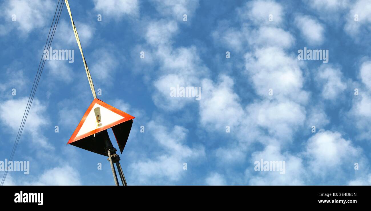 Rotes Dreieck mit Ausrufezeichen auf Stahlseil von elektrischem Pylon, flauschiger Himmel im Hintergrund - breites Foto, Platz für Text rechts Stockfoto
