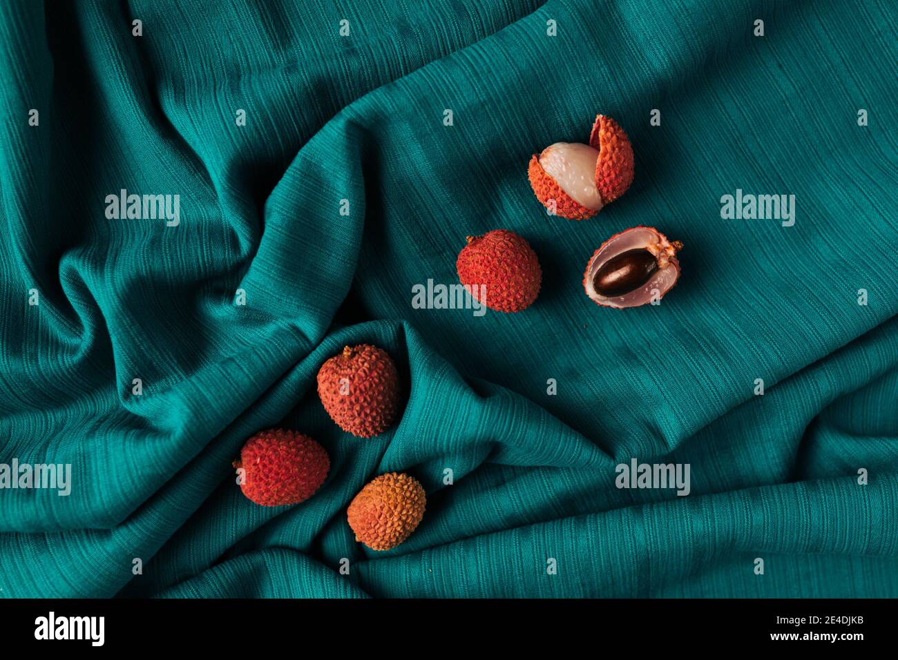 Ästhetisches Layout von frischem Bio-Lychee (Litchi Fruit) vor dunkelcyanfarbenem Stoffhintergrund. Stockfoto