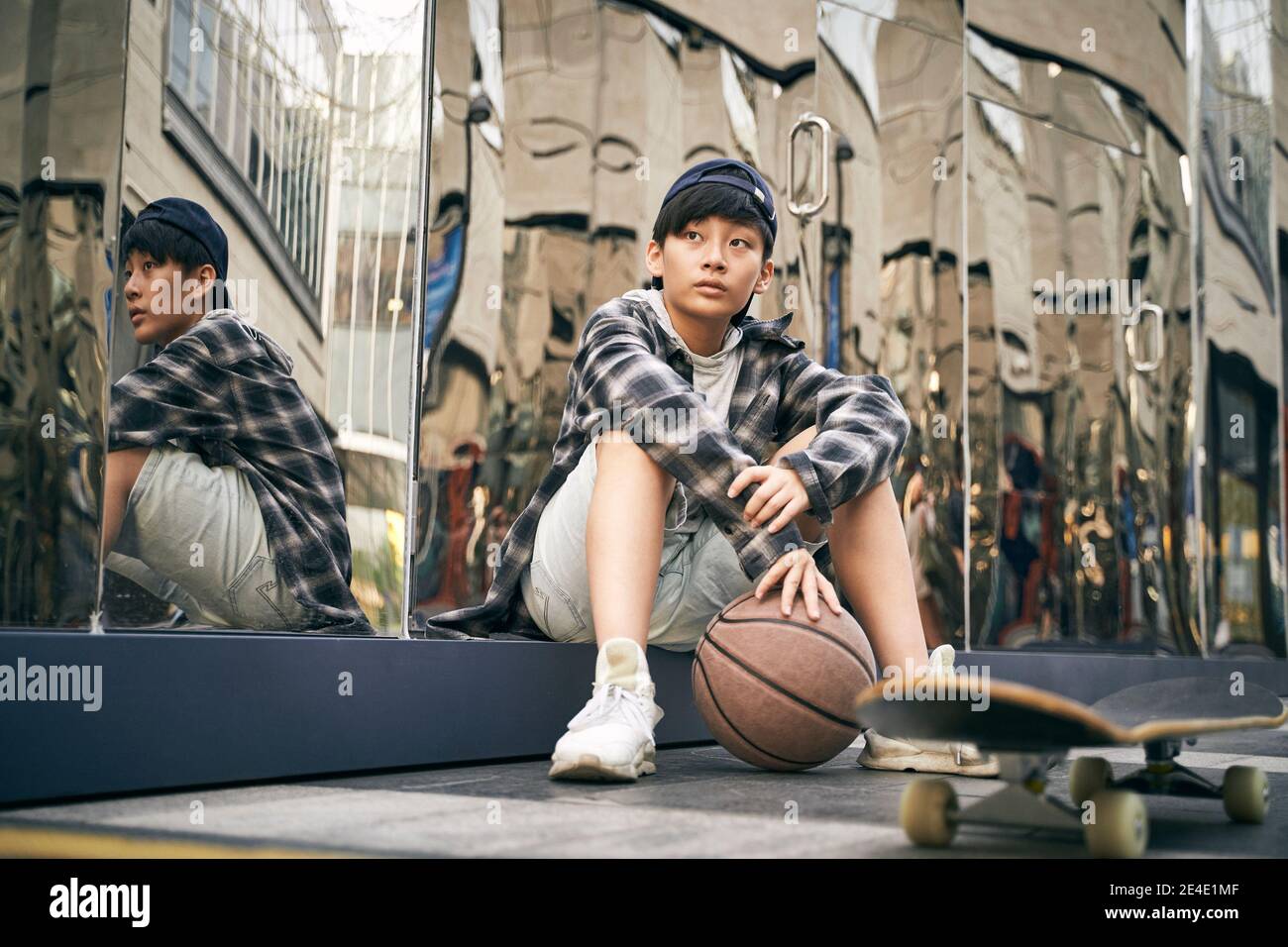 Teenager asiatische Kind unter ein Pause sitzen auf Boden mit Basketball und Skateboard Stockfoto
