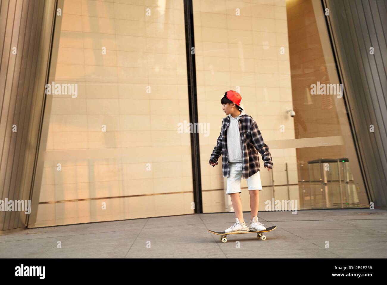 15-jähriger asiatischer Teenager-Skateboarding vor dem modernen Gebäude Stockfoto