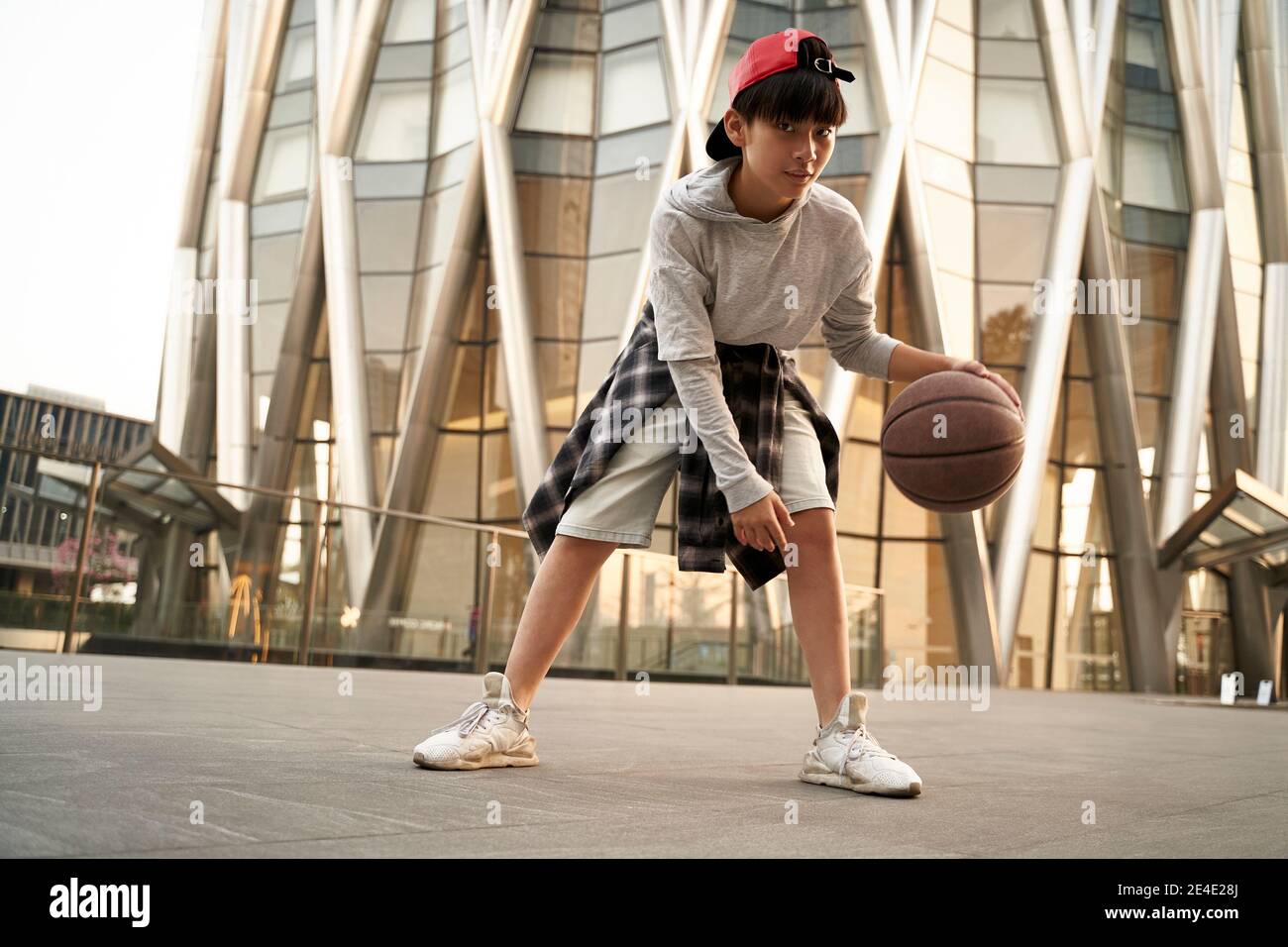 15-jähriger asiatischer Teenager-Junge spielt Basketball im Freien vor Ein modernes Gebäude Stockfoto