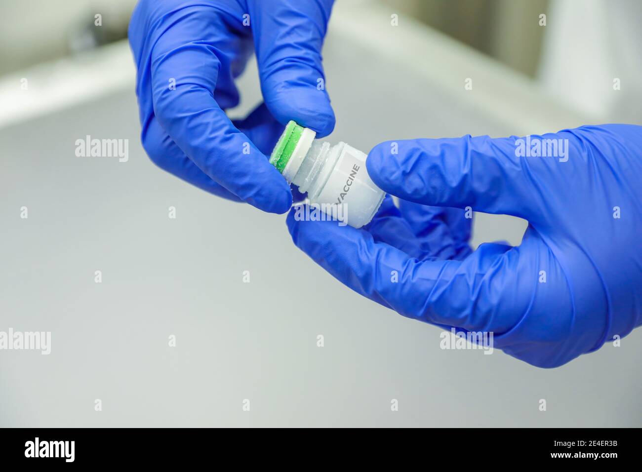 Hand mit einem medizinischen Handschuh, der eine Flasche Impfstoff aus der Eislagerung hält. Medikamentöse Behandlung bei Stickstoffeinfrieren. Stockfoto