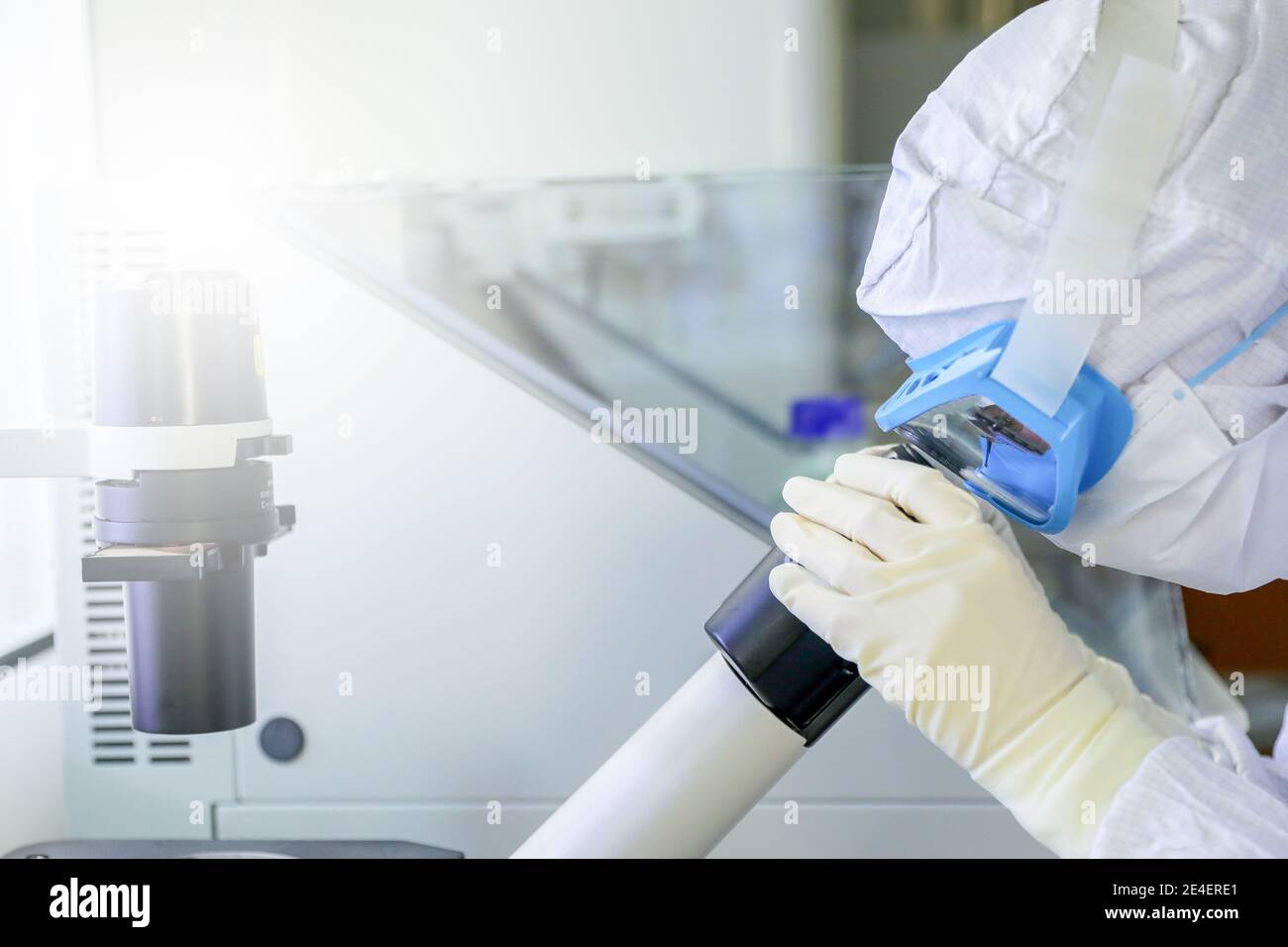 Laborwissenschaftler tragen Schutzkleidung auf der Suche nach Mikroskopen, während sie medizinische Forschung in einem Labor betreiben. Stockfoto