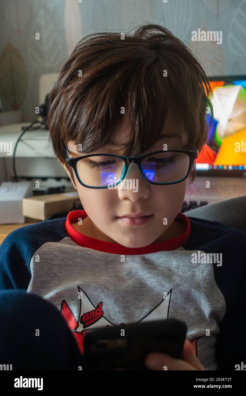 Ein Junge trägt eine blaue Brille, um seine Augen vor UV-Licht zu schützen, während er auf einem Handy auf einem Spiel spielt. Stockfoto