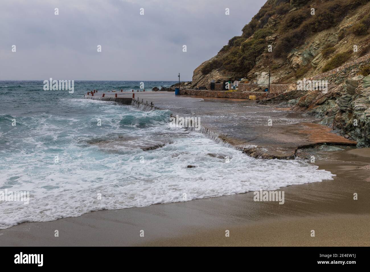 Agkali Beach, Folegandros Island, Griechenland - 24. September 2020: Ein Betonkai an einem Sandstrand, überflutet von den Wellen des rauen Meeres. Stockfoto