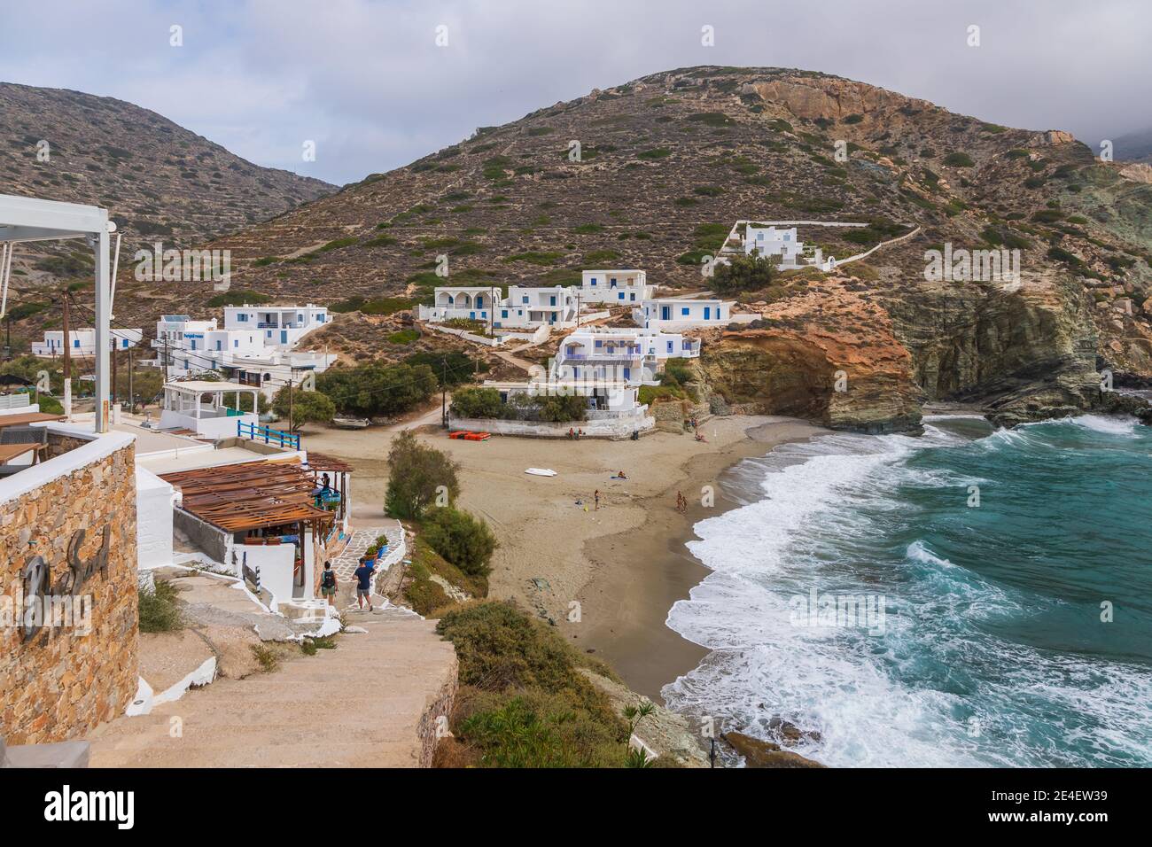 Agkali Beach, Folegandros Island, Griechenland - 24. September 2020: Weiße Villen am Hang neben einem Sandstrand. Touristen schwimmen im Meer und entspannen auf Stockfoto