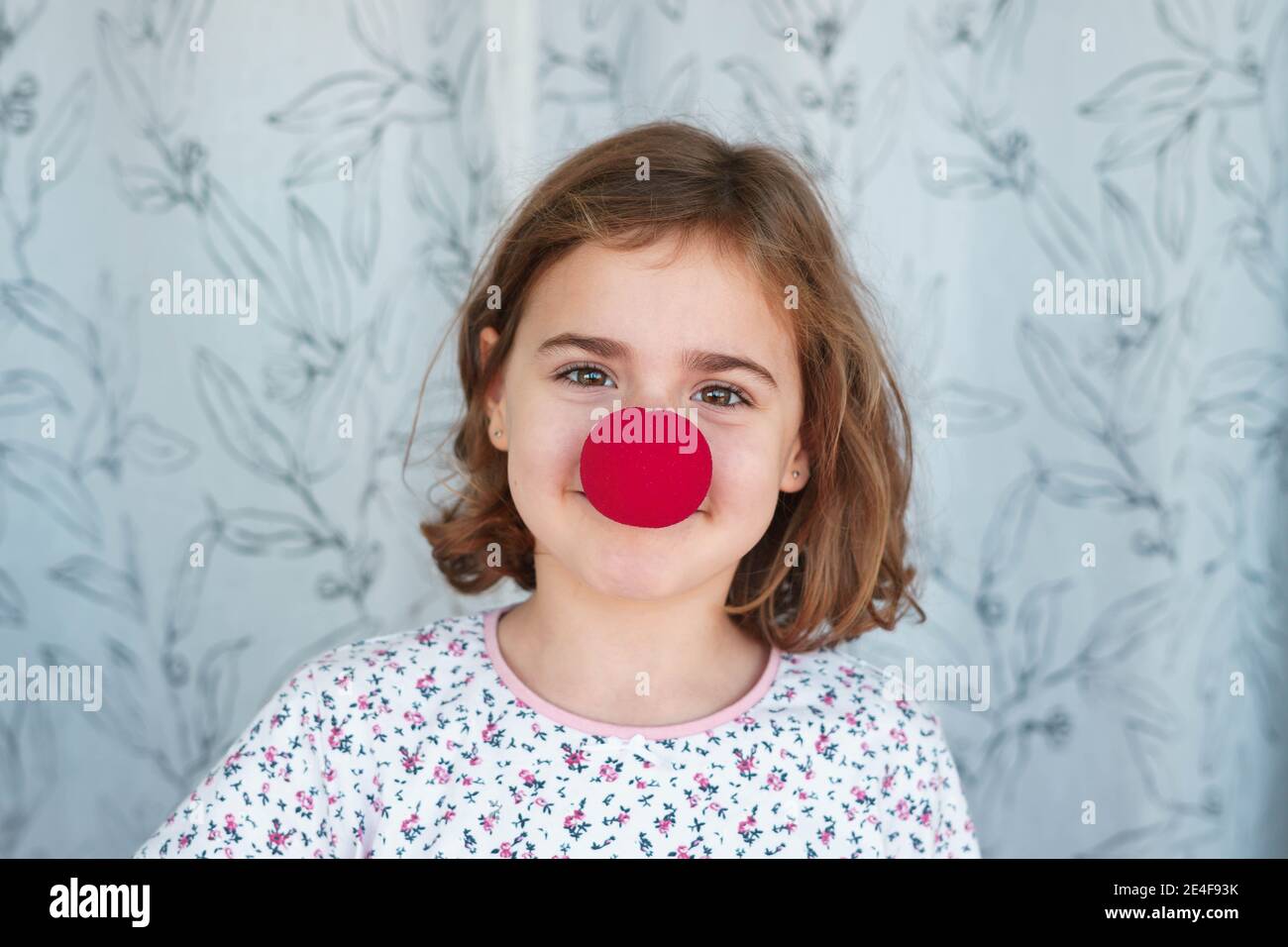 Portrait von lächelndes Mädchen mit roten Clown Nase. Portrait zu Hause mit selektivem Fokus. Konzept von Freude und Spaß. Stockfoto