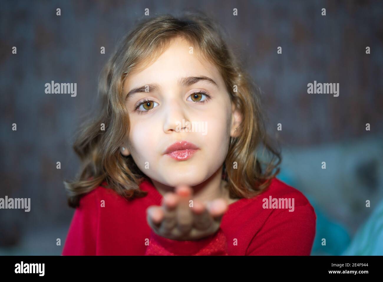 Kleines Mädchen sendet einen Kuss mit der Hand an die Kamera, Porträt mit selektivem Fokus. In roten Pullover gekleidet. Stockfoto