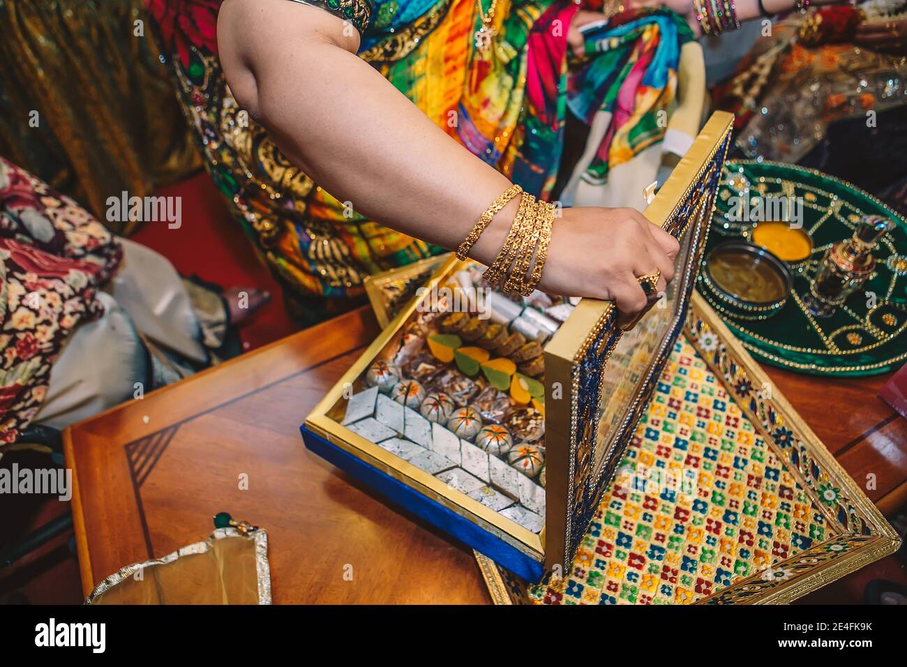 Weibliche Hand mit goldenen Armbändern öffnen Luxus-Box mit traditionellen Süßigkeiten auf Henna mehndi sangeet Party Stockfoto