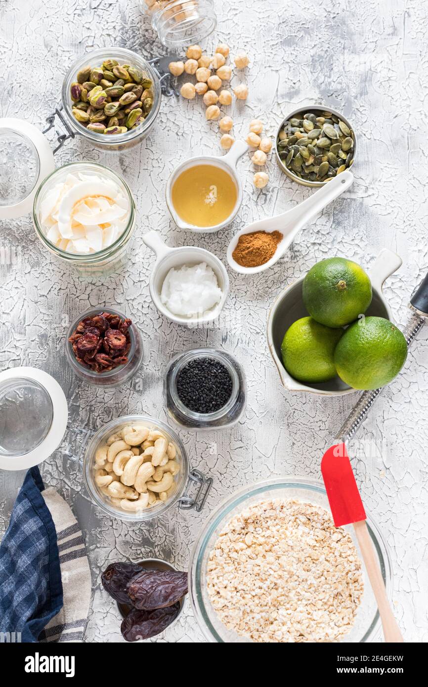 Overhead-Ansicht von einigen rohen Granola Zutaten in Gläsern und Schalen über einem rustikalen grauen und weißen Hintergrund. Stockfoto