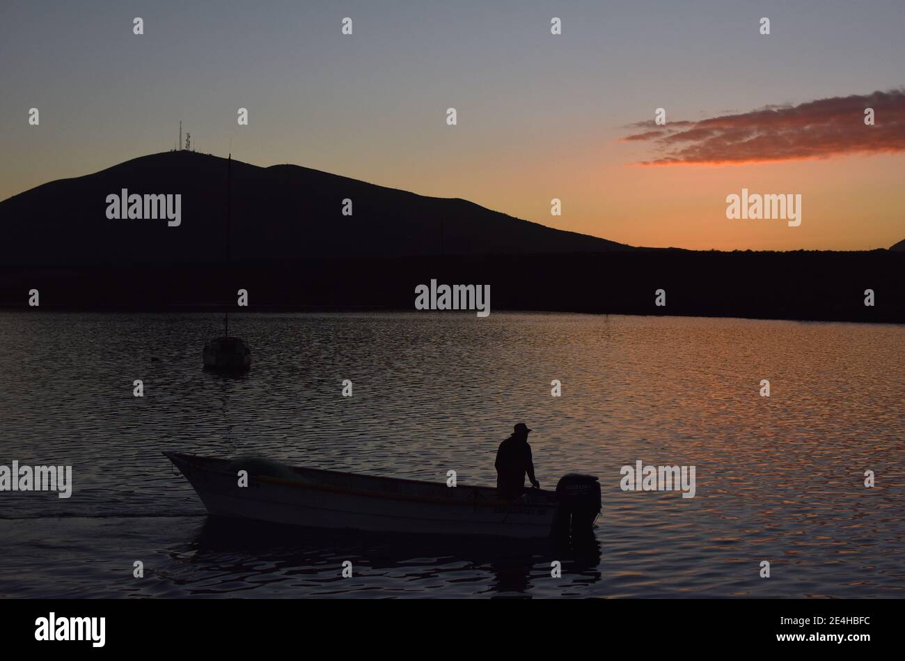 Ein Einzelboot und ein Fischer haben am Hafen von San Quintin in Baja California bei Molino Viejo den Sonnenuntergang im Hintergrund dargestellt Stockfoto