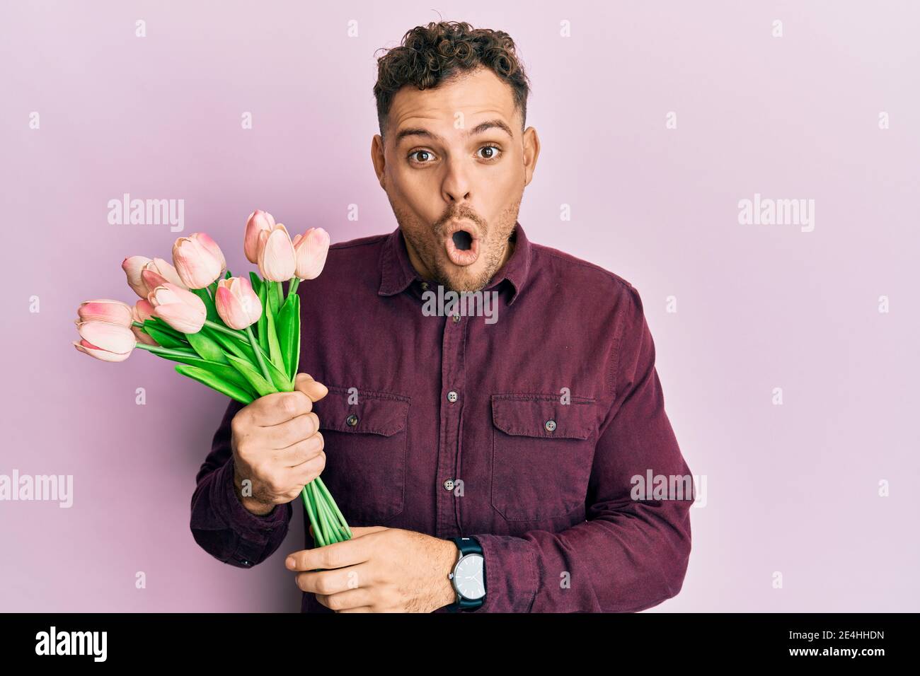 Junger hispanischer Mann hält Bouquet von rosa Tulpen Blumen verängstigt und erstaunt mit offenem Mund für Überraschung, Unglauben Gesicht Stockfoto