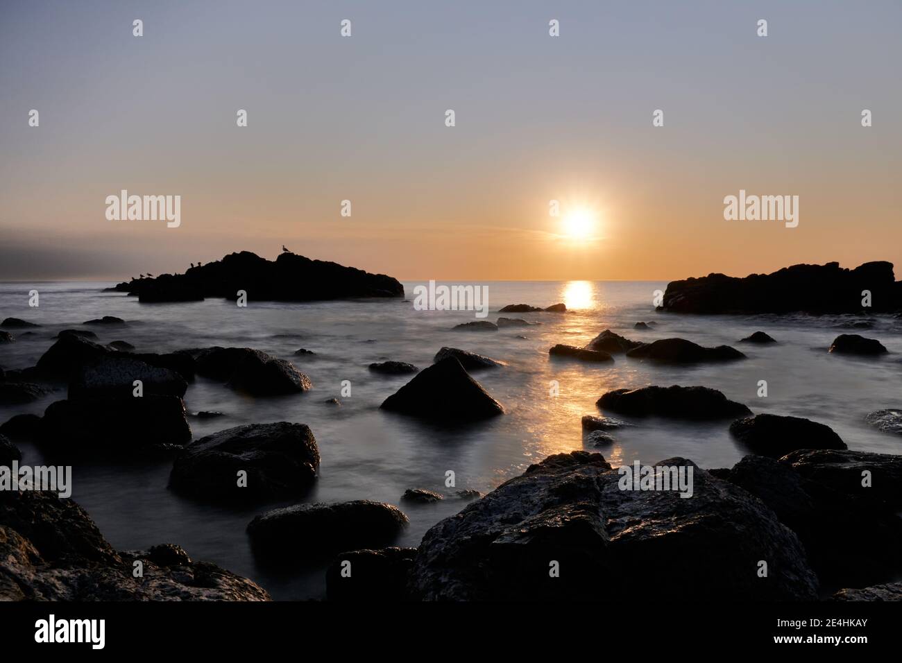 Eine lange Sicht auf die Küste Strand: Die Farben des Sonnenuntergangs auf dem Wasser die Felsen und den Himmel Stockfoto