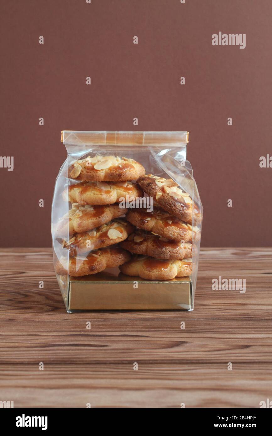 Shortbread-Kekse mit Mandelflocken in transparentem Beutel auf einem Holztisch gegen braune Wand. Nahaufnahme Stockfoto